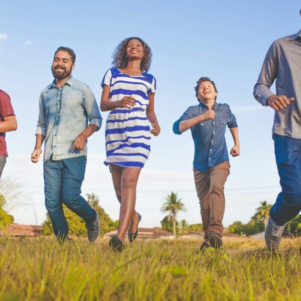 Group of five diverse friends running in a field with smiles